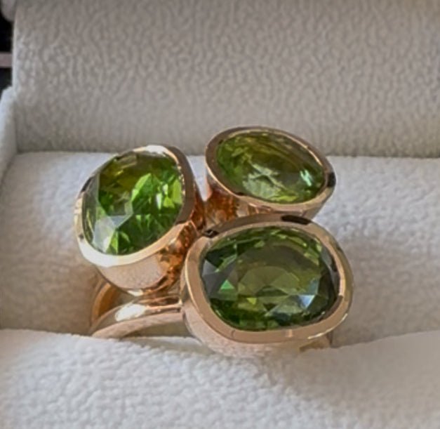 Handgjord cocktailring i 18k guld med tre gröna peridoter på vit bakgrund