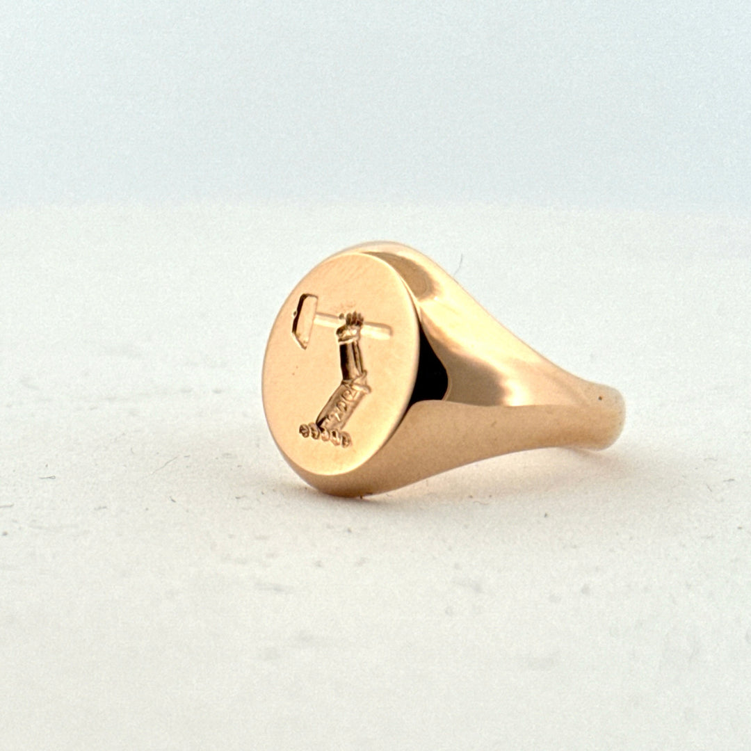 Guldklackring med handgraverat motiv, visad i profil på ljus bakgrund