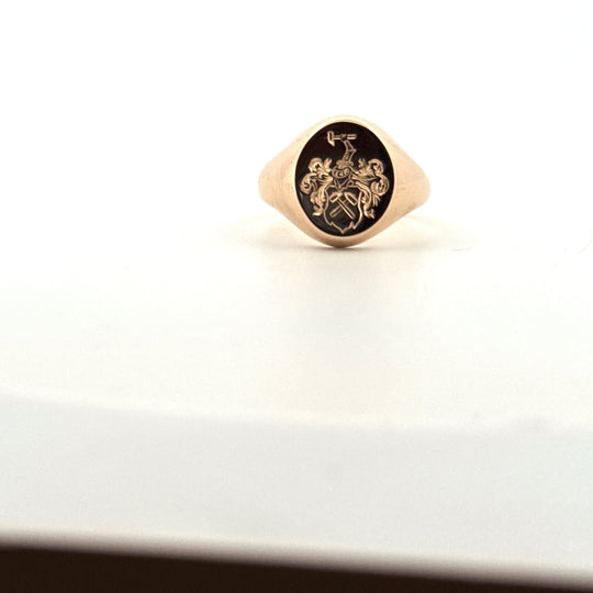 Klackring i guld med handgraverat vapentecken, närbild på ljus bakgrund