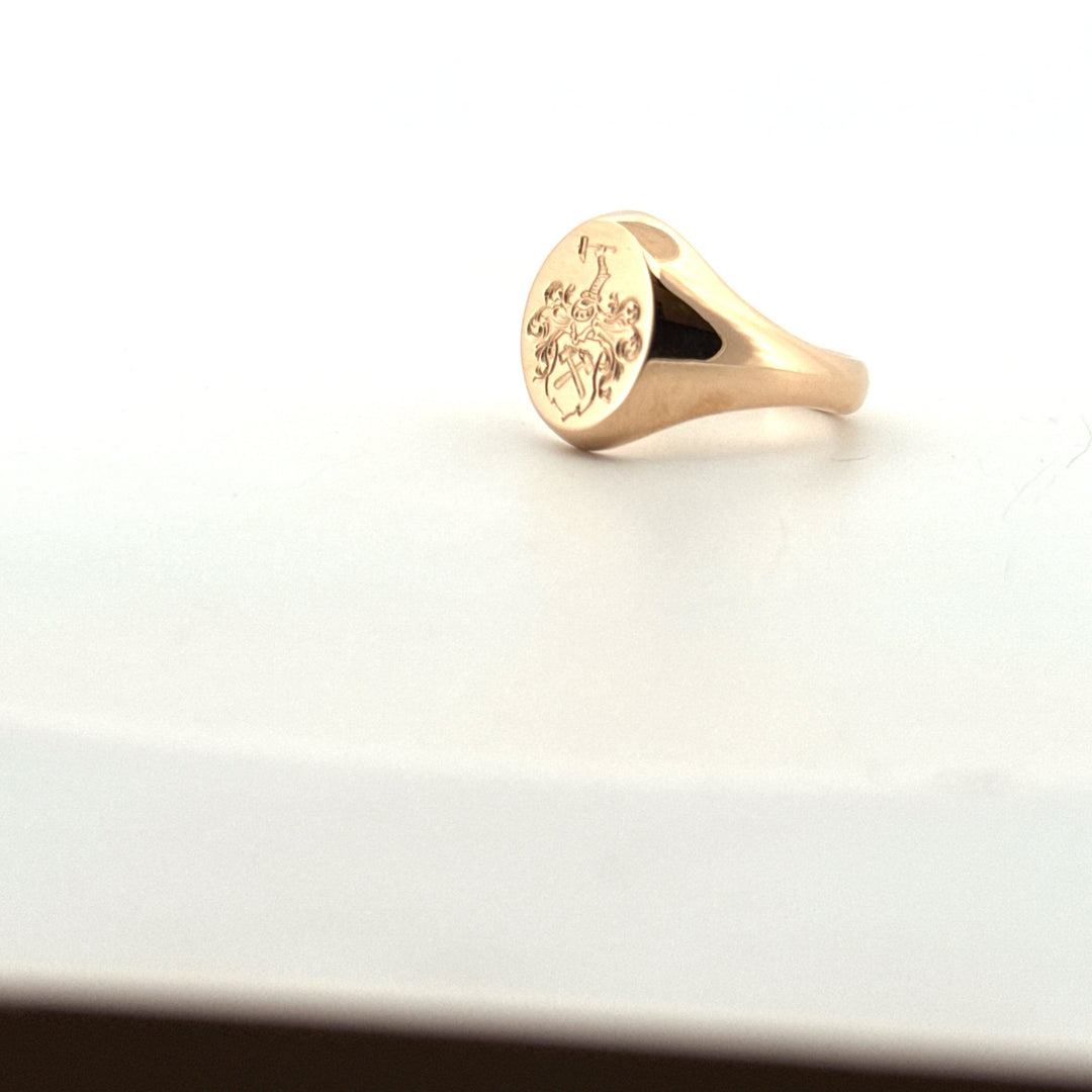 Handgjord klackring i guld med vapengravyr, lutad framåt för att visa motivet