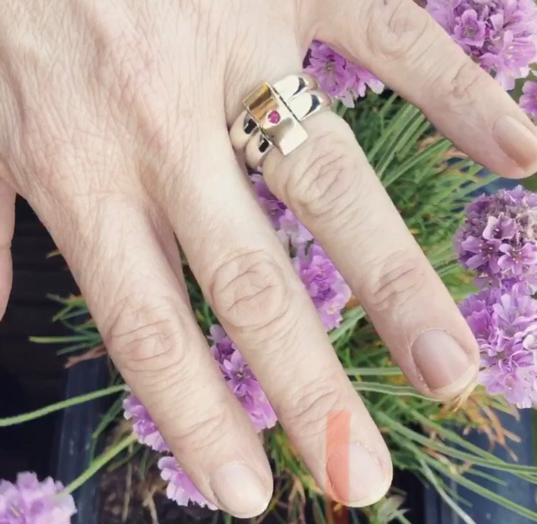 Vändbar ring i guld buren på hand, visad utomhus bland lila blommor – Ett Rum För Smycken